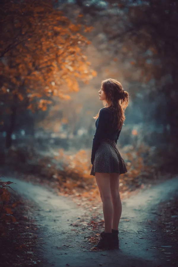 A woman standing at a fork between two paths in an autumn park, deciding which way to go